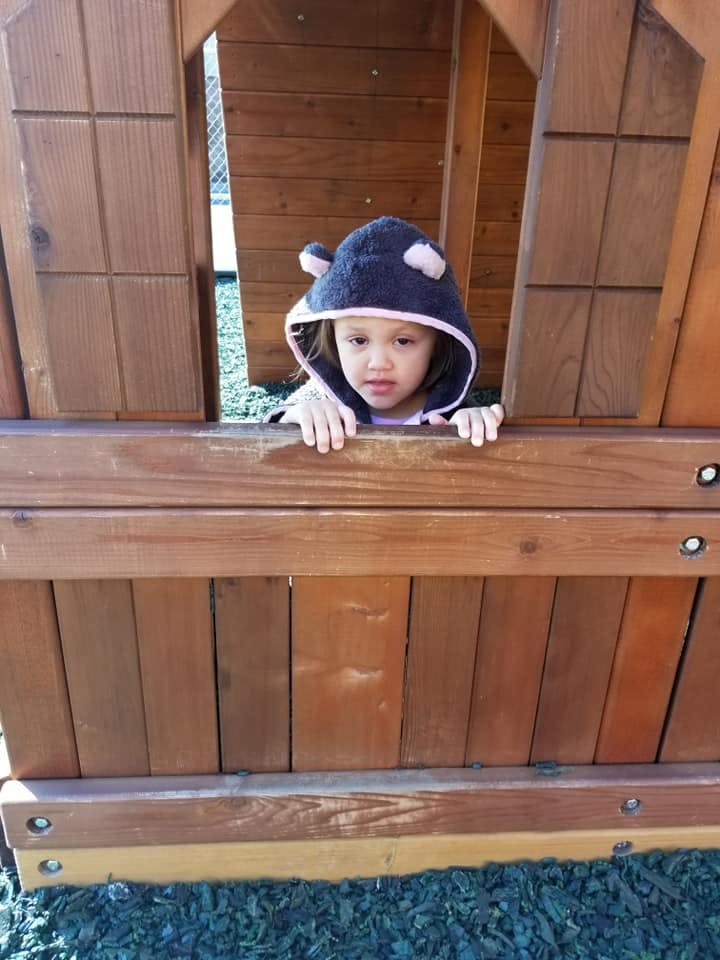 Child in a hooded top looking out from a wooden play structure