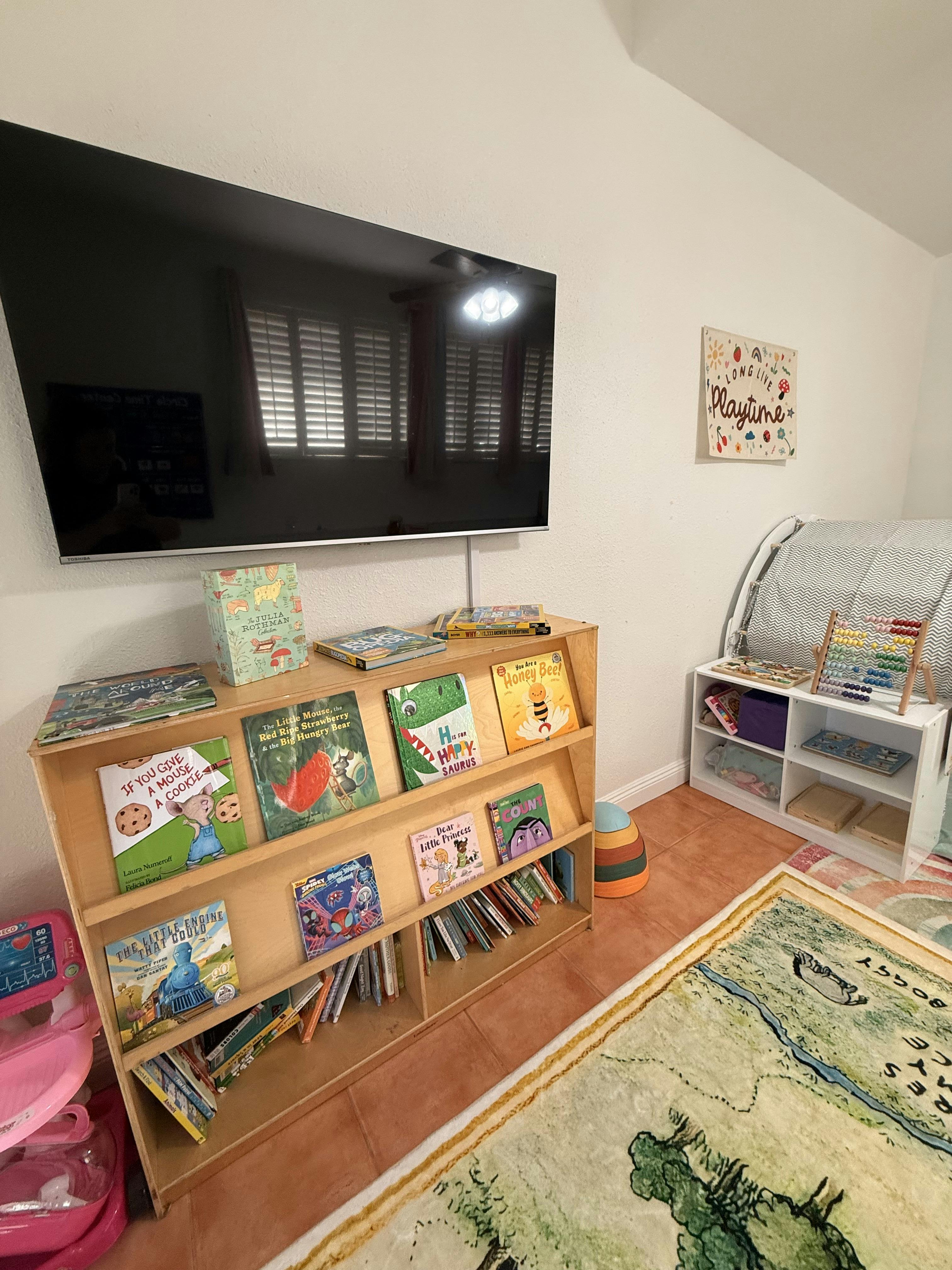Wooden bookcase filled with children's books below a wall mounted television