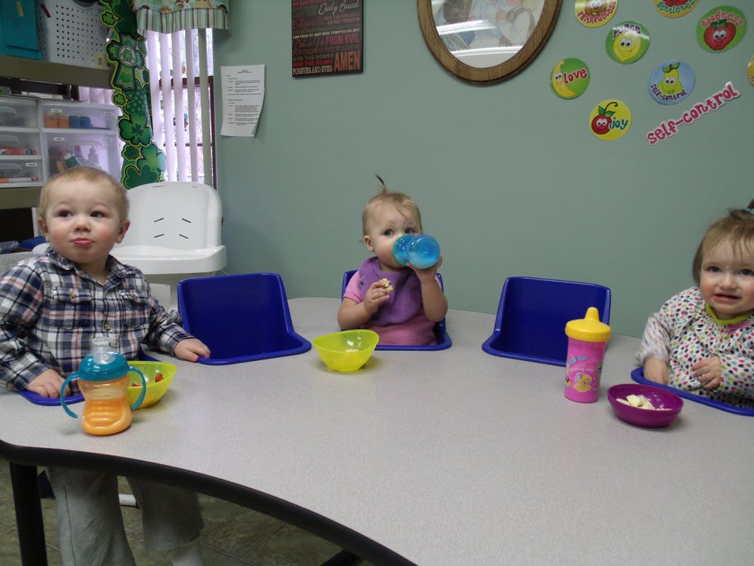 Three children sitting at a table with bowls and sippy cups