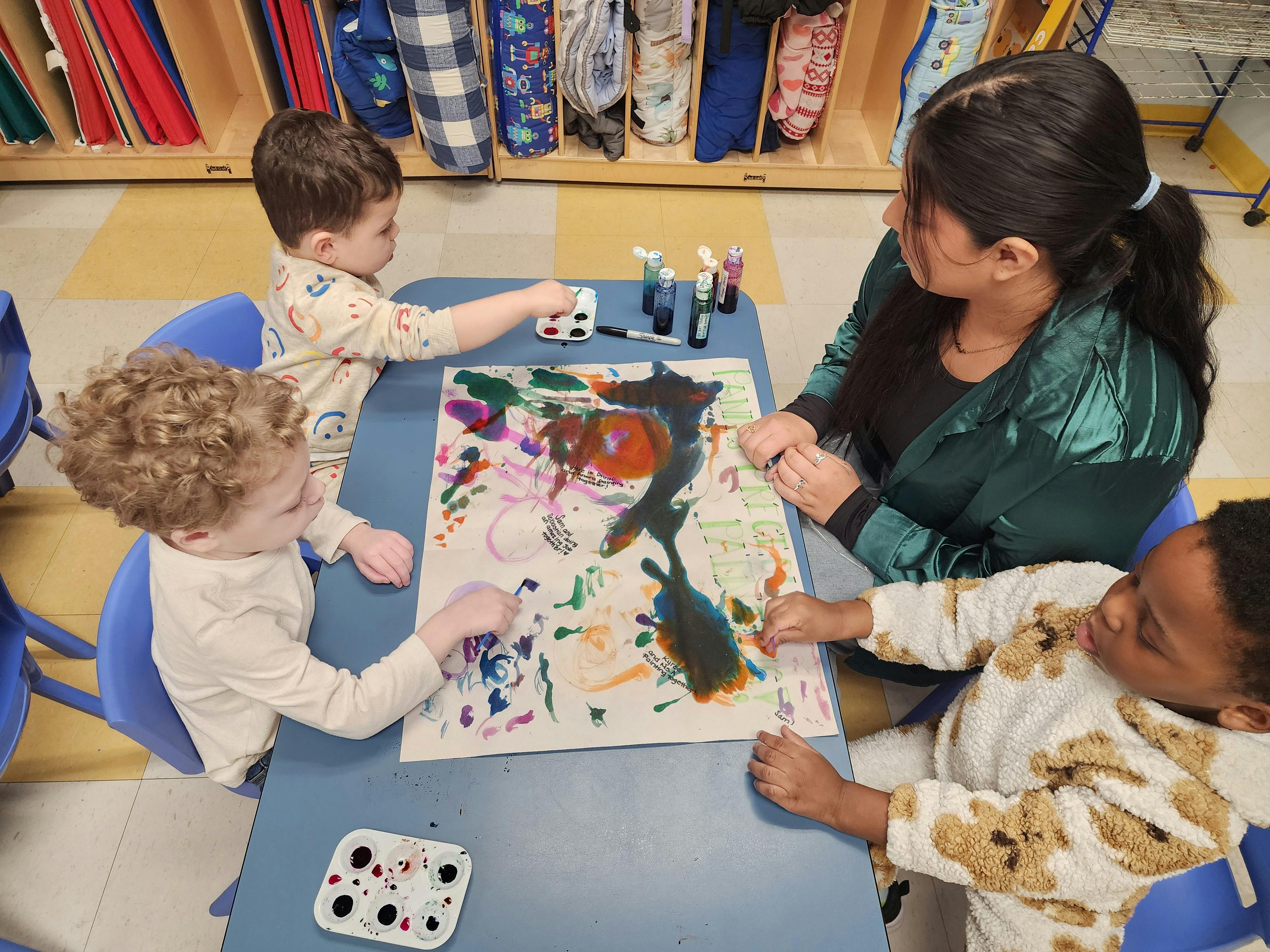 Adult and three children painting on a large sheet of paper at a table