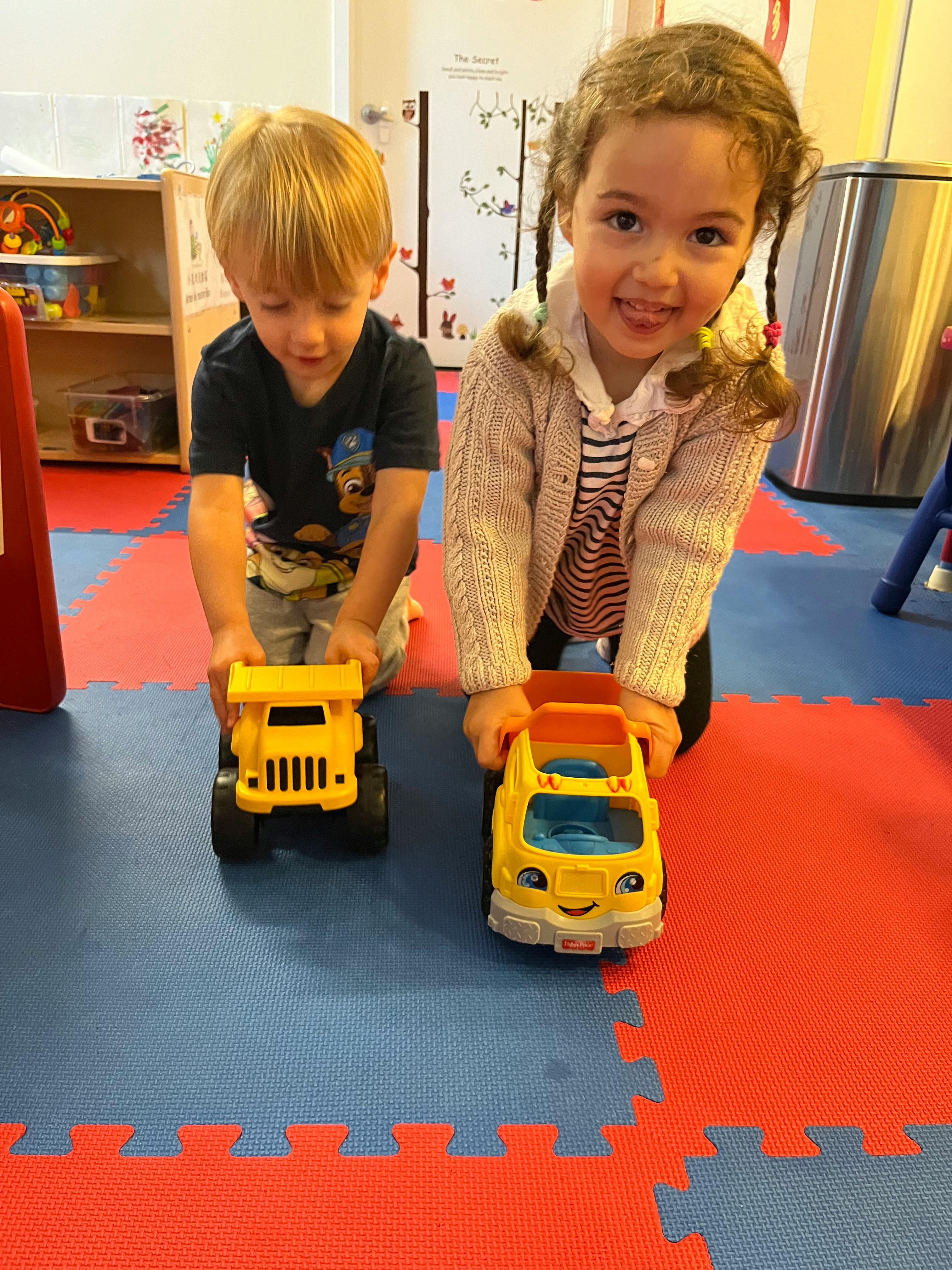 Two children playing with toy trucks on a colorful mat