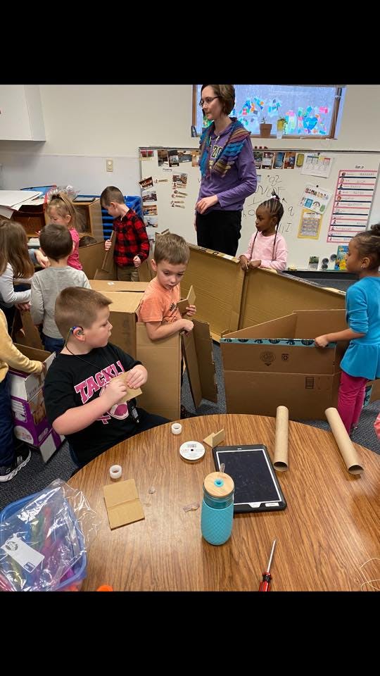 Adult and children in a classroom building structures with cardboard boxes