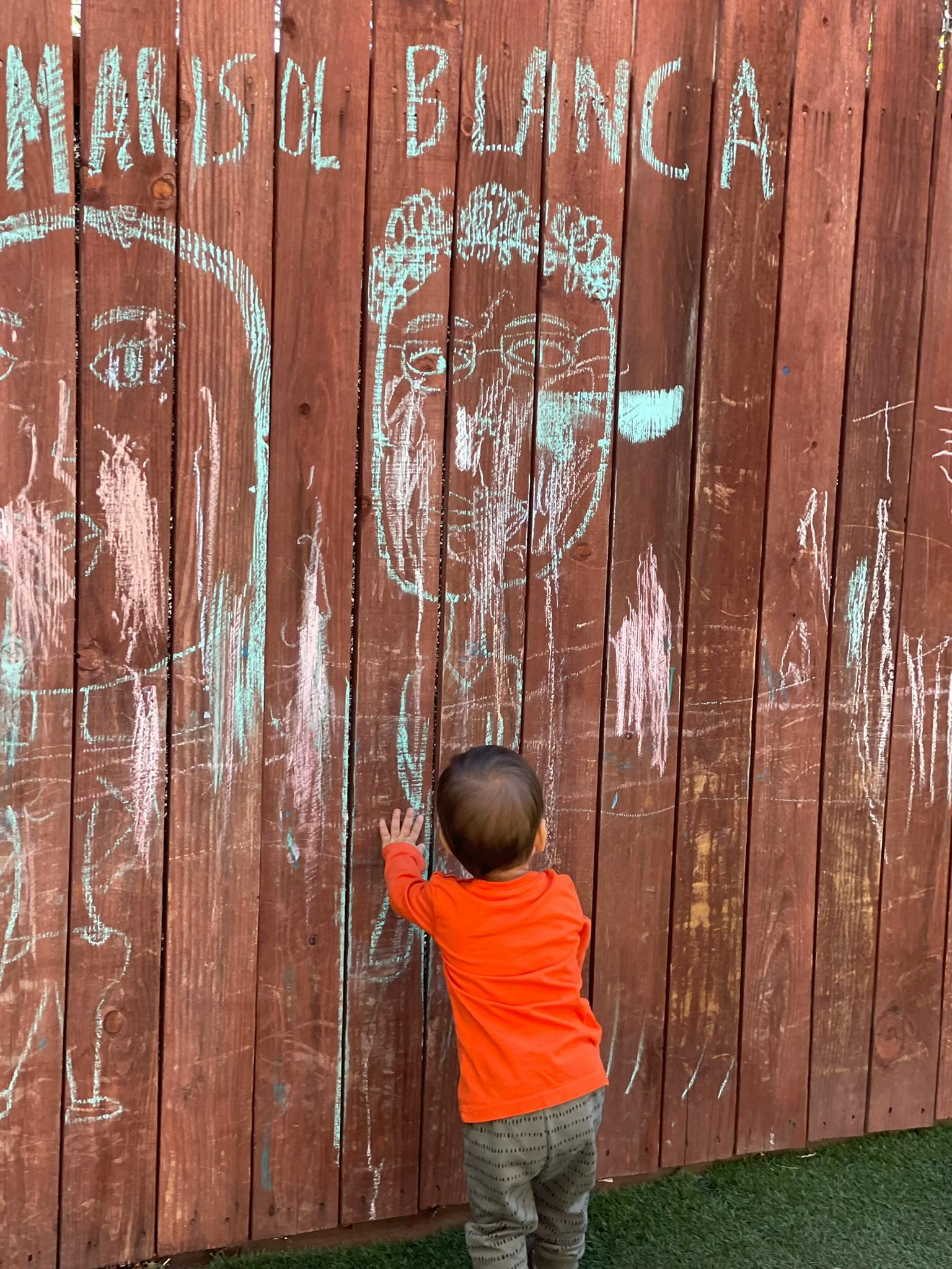 Child in orange shirt drawing on a wooden fence with chalk