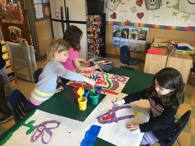 Three children painting at a table in a classroom