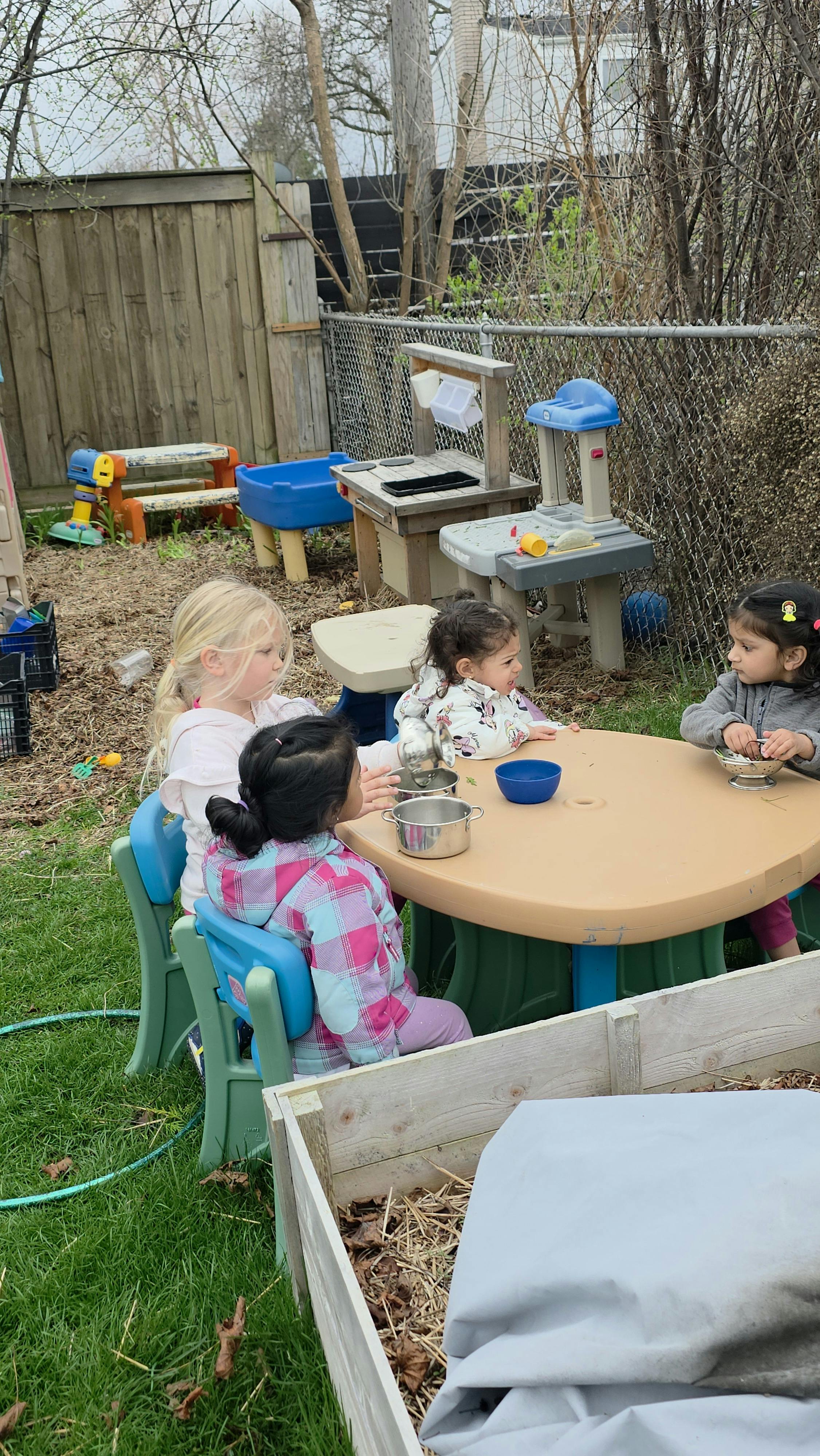 Four children sitting at a round table playing with toy kitchen supplies