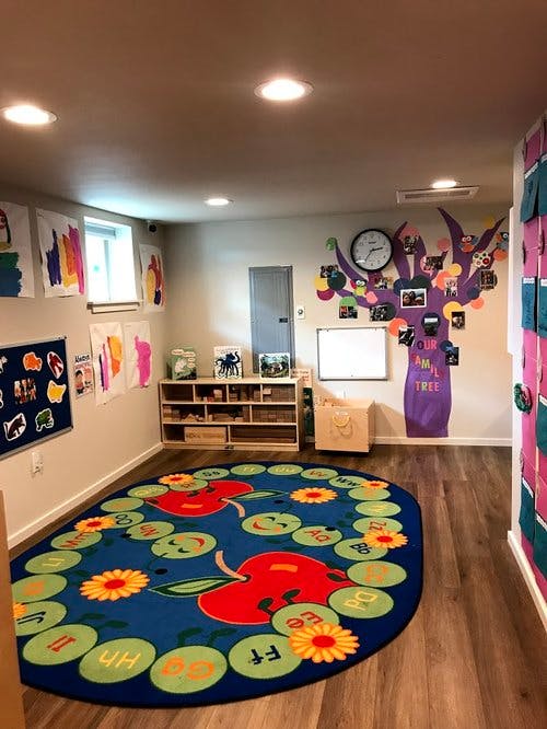 Classroom with a large blue rug with apples and flowers, and artwork on the walls