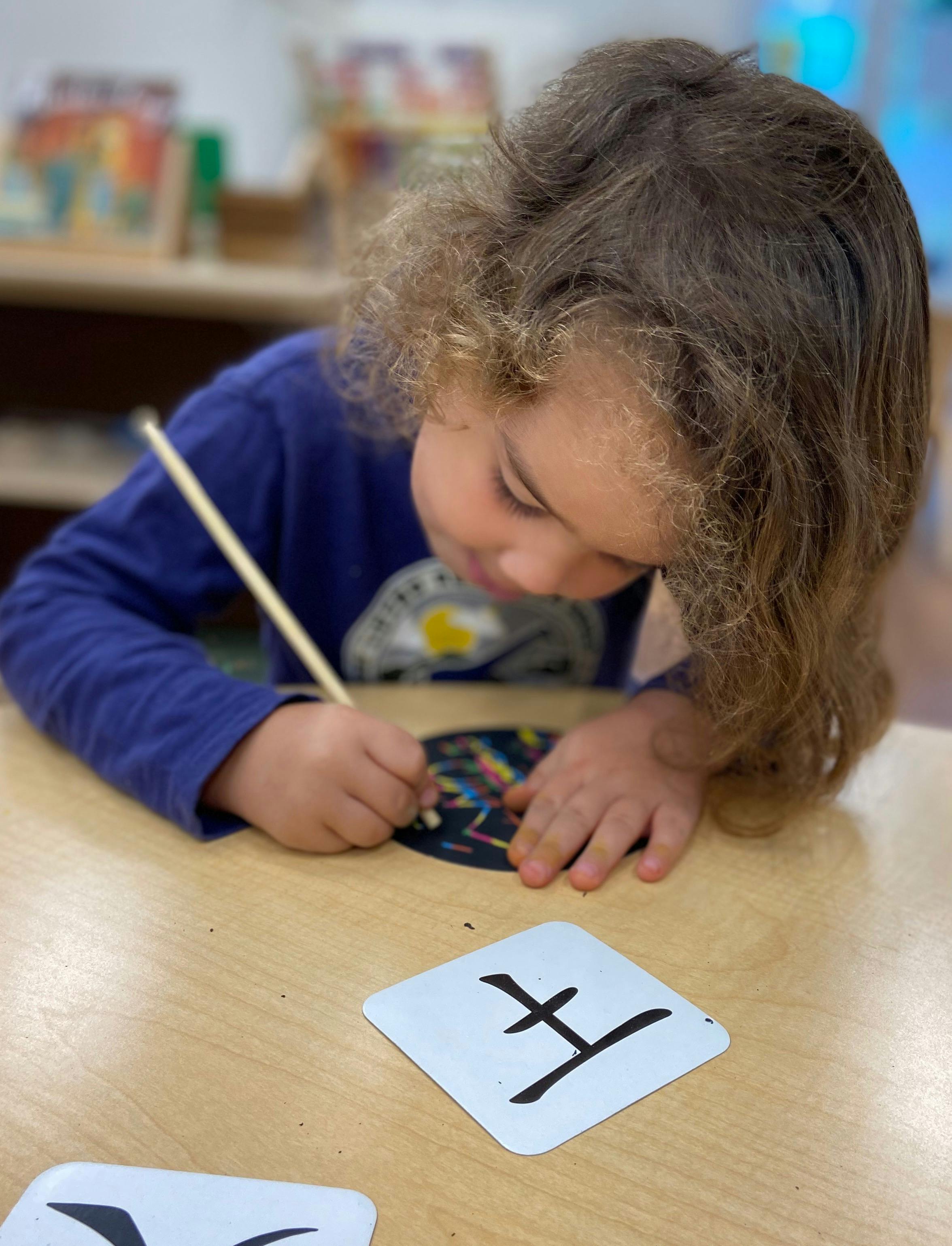 Child drawing with a stylus on a scratch art surface at a table