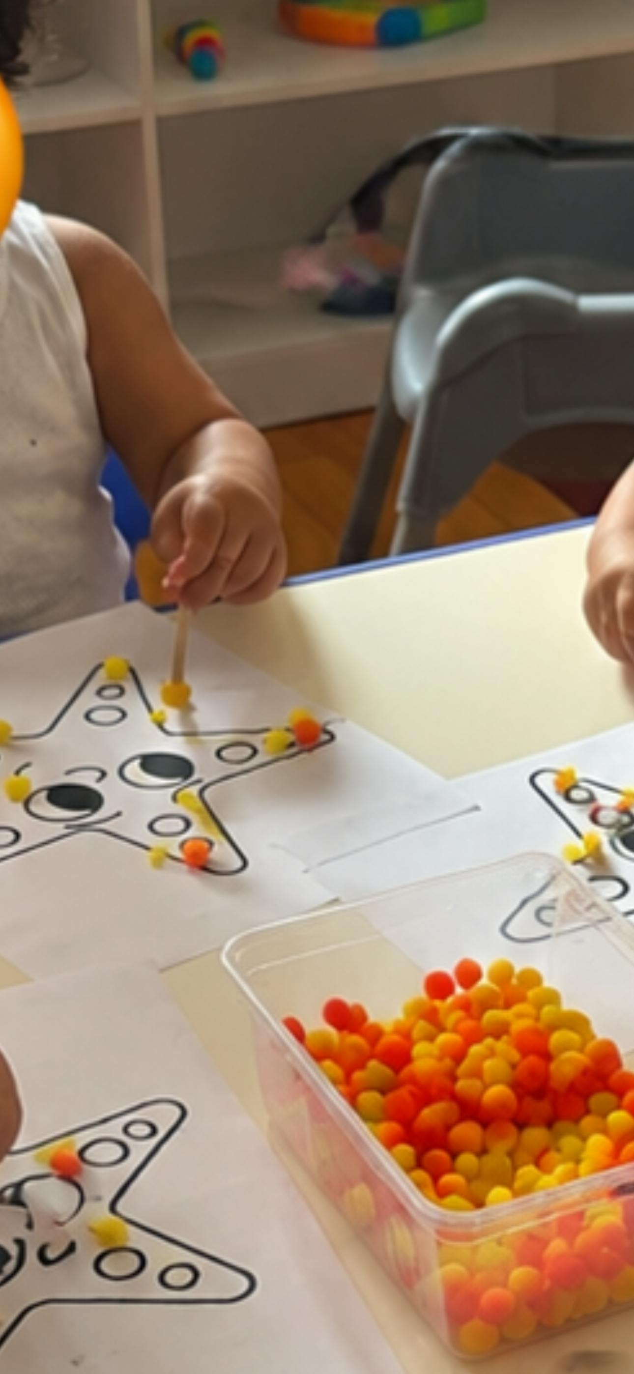 Child placing small colorful pom-poms onto a starfish coloring page