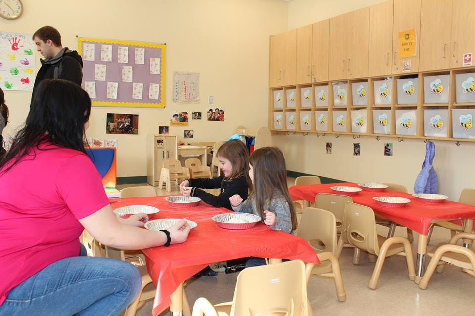 Adult and two children sitting at a table with plates in a classroom