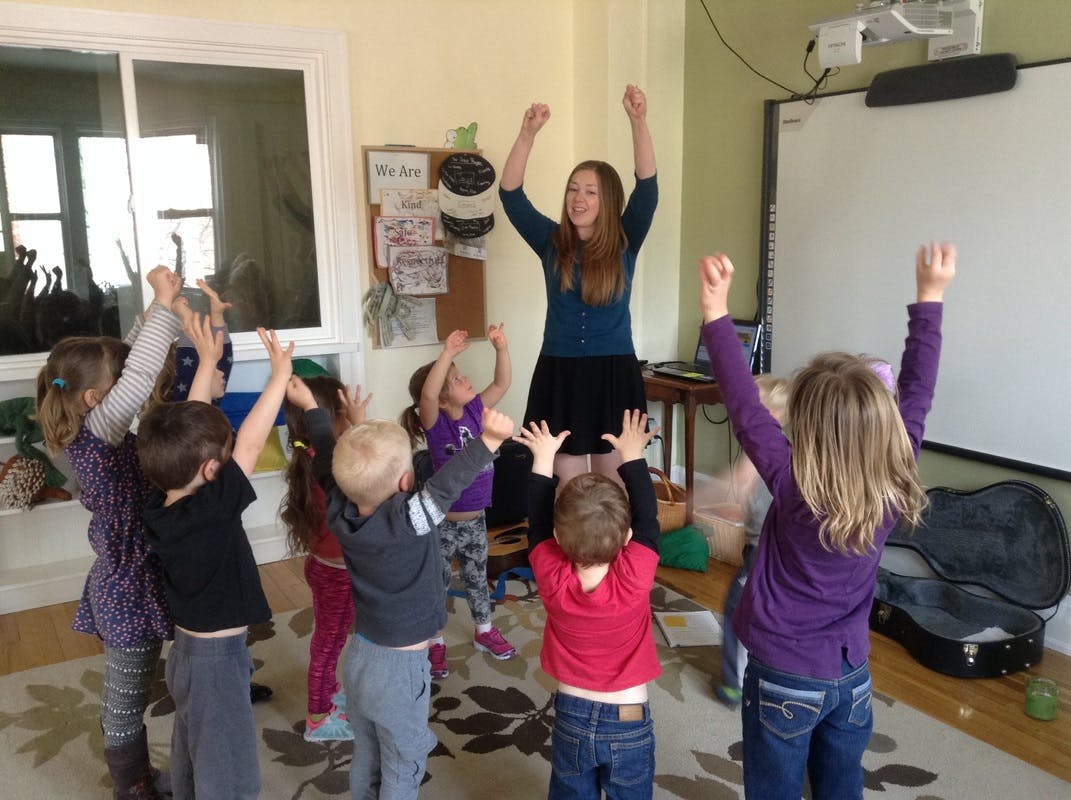 Adult and children with arms raised in a classroom