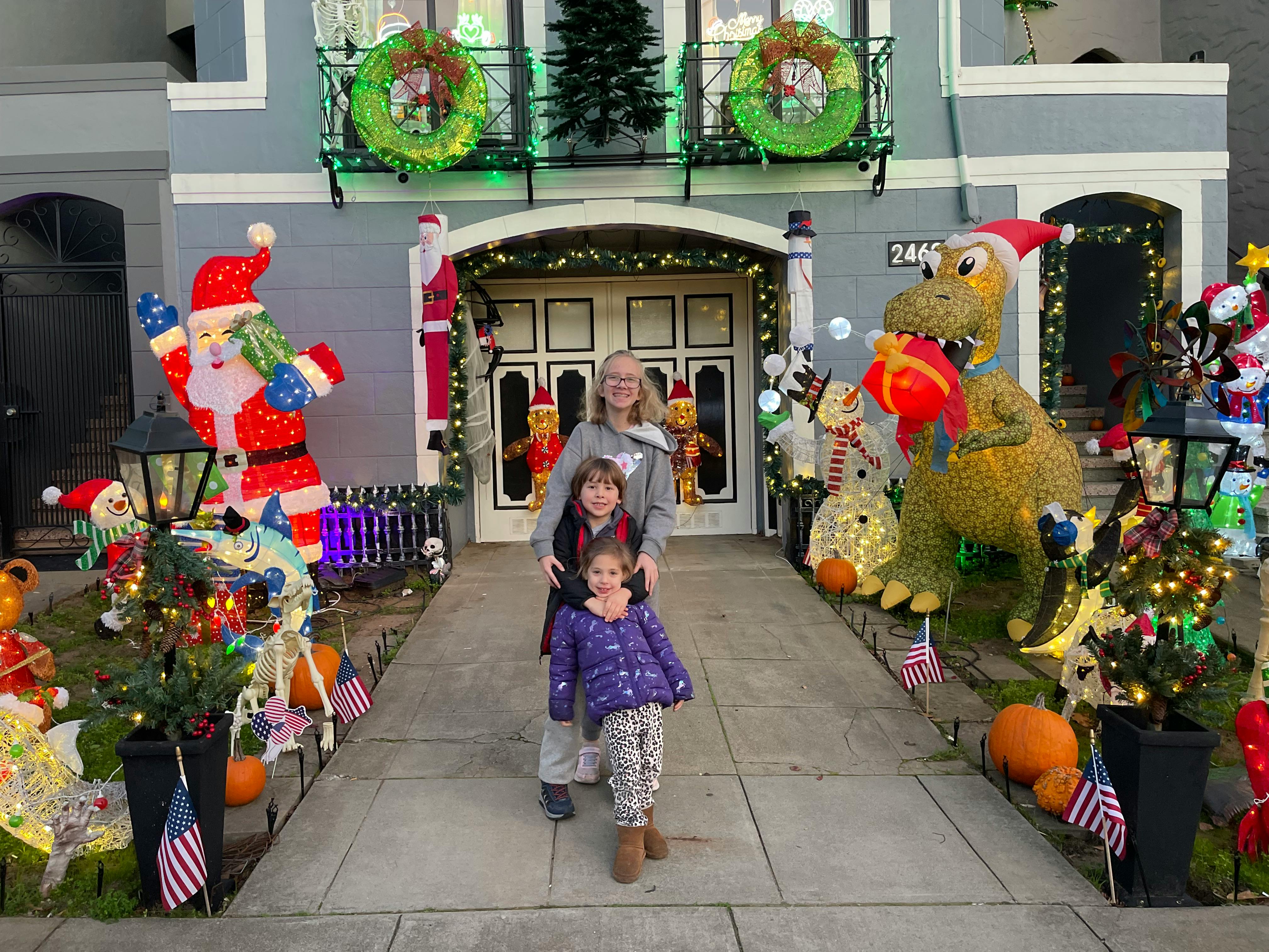 Person and two children standing in front of a house with holiday decorations