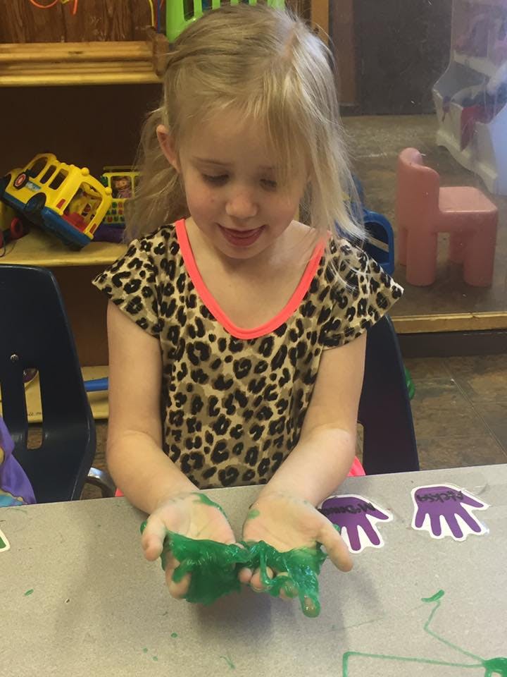 Child playing with green slime at a table