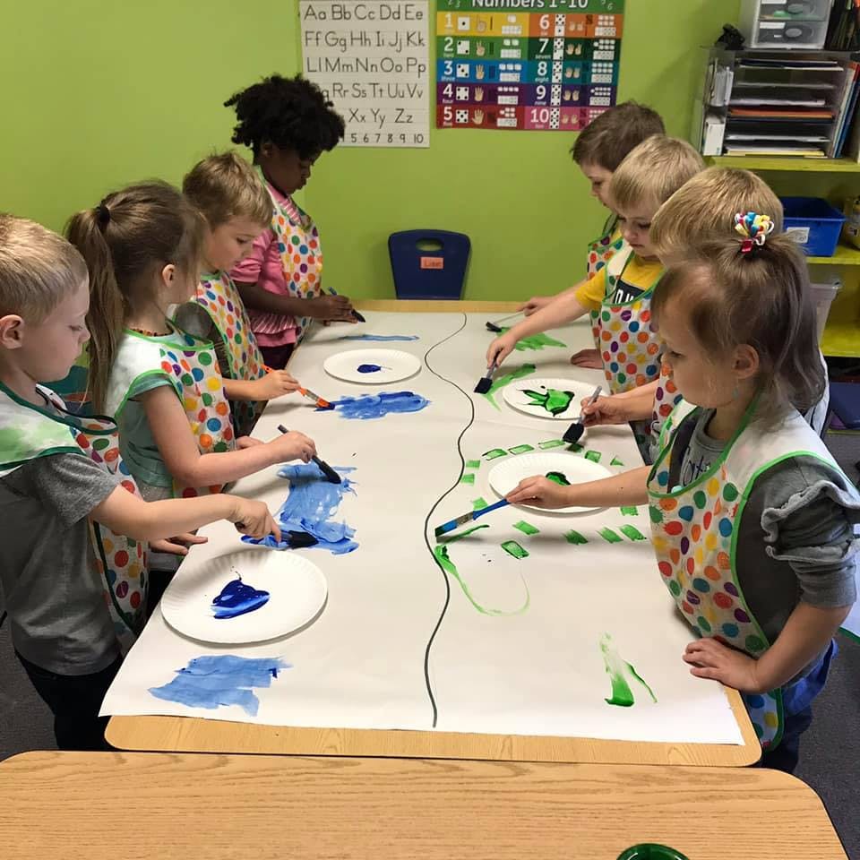 Children painting at a table in a classroom