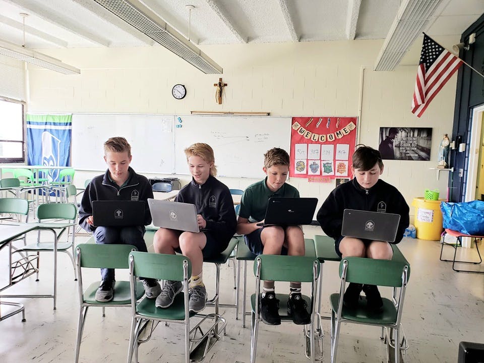 Four children sitting on chairs using laptops in a classroom