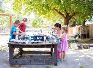 Children playing with pots and pans at a table outdoors