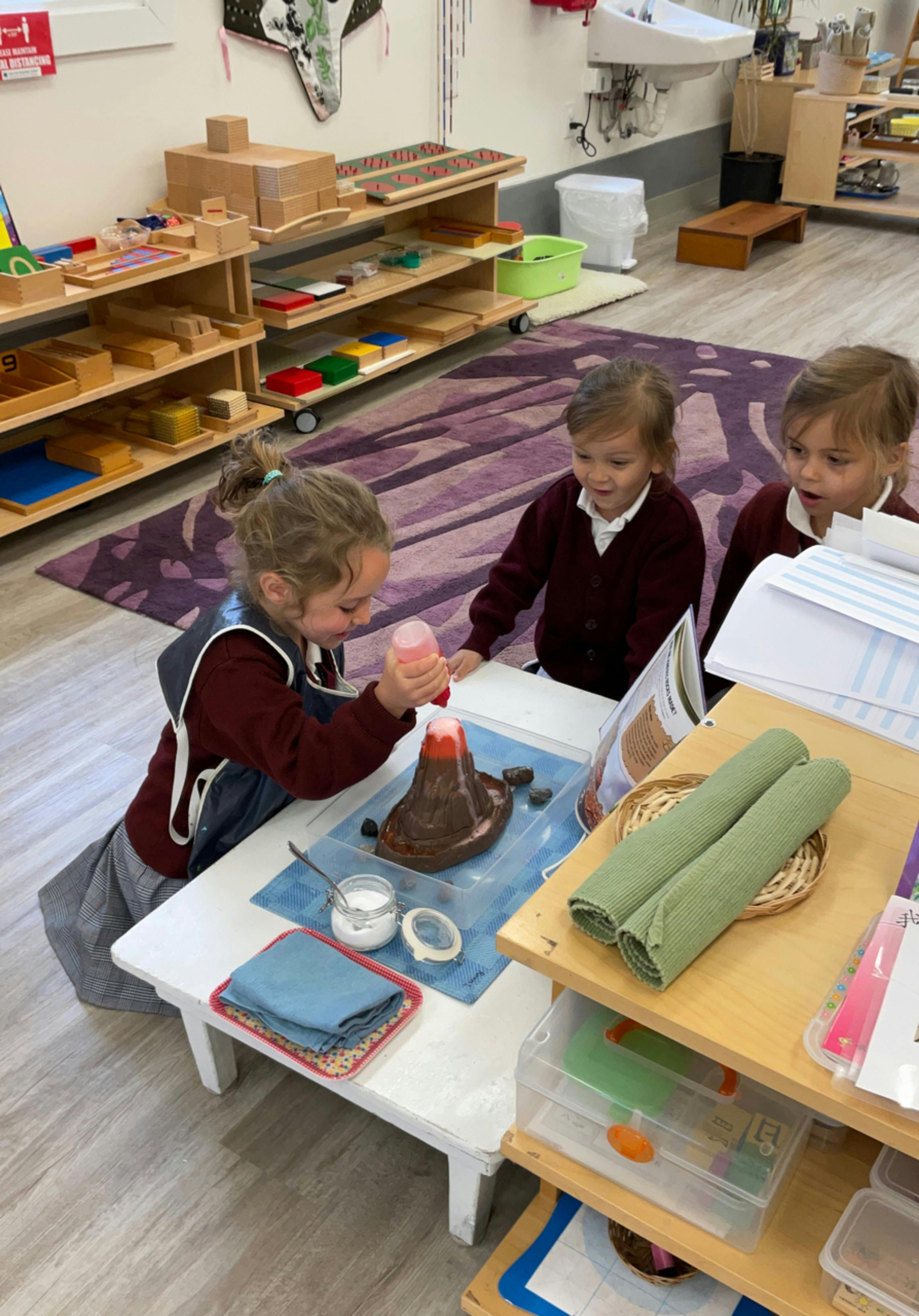 Three children doing a volcano experiment in a classroom