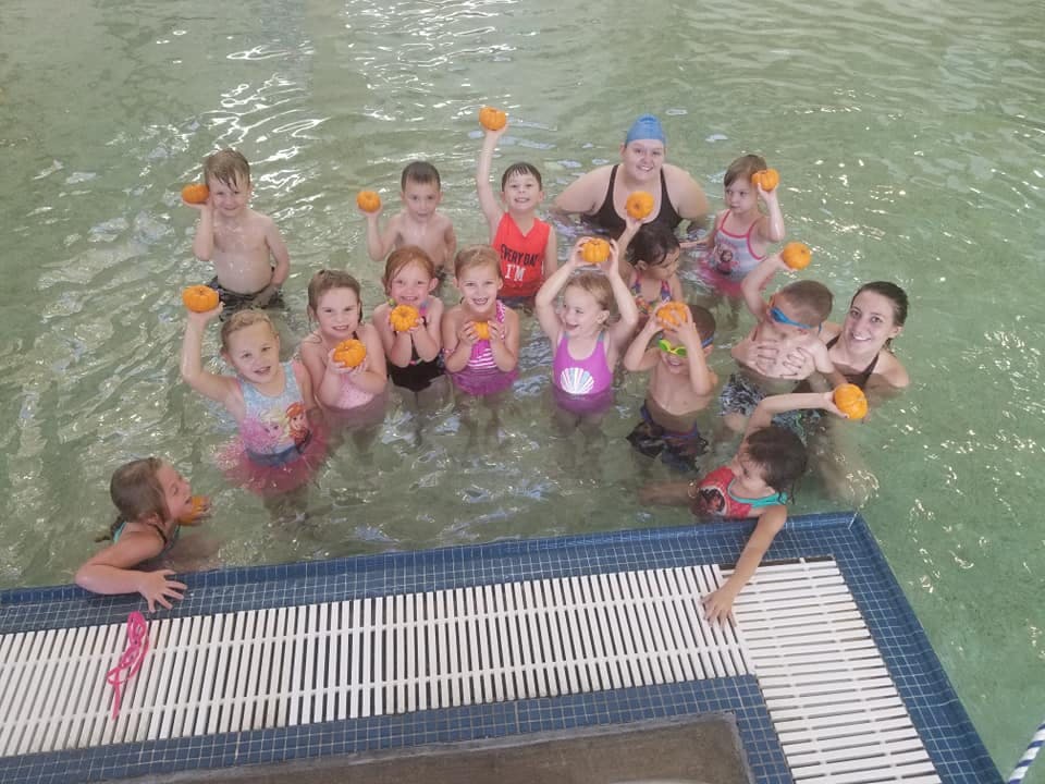 Group of children and adults in a swimming pool holding orange objects