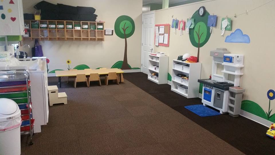 Empty classroom with small tables and chairs, shelves, and play kitchen