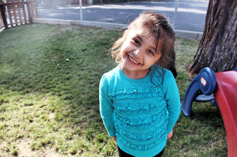 Child in a blue shirt smiling in a grassy area