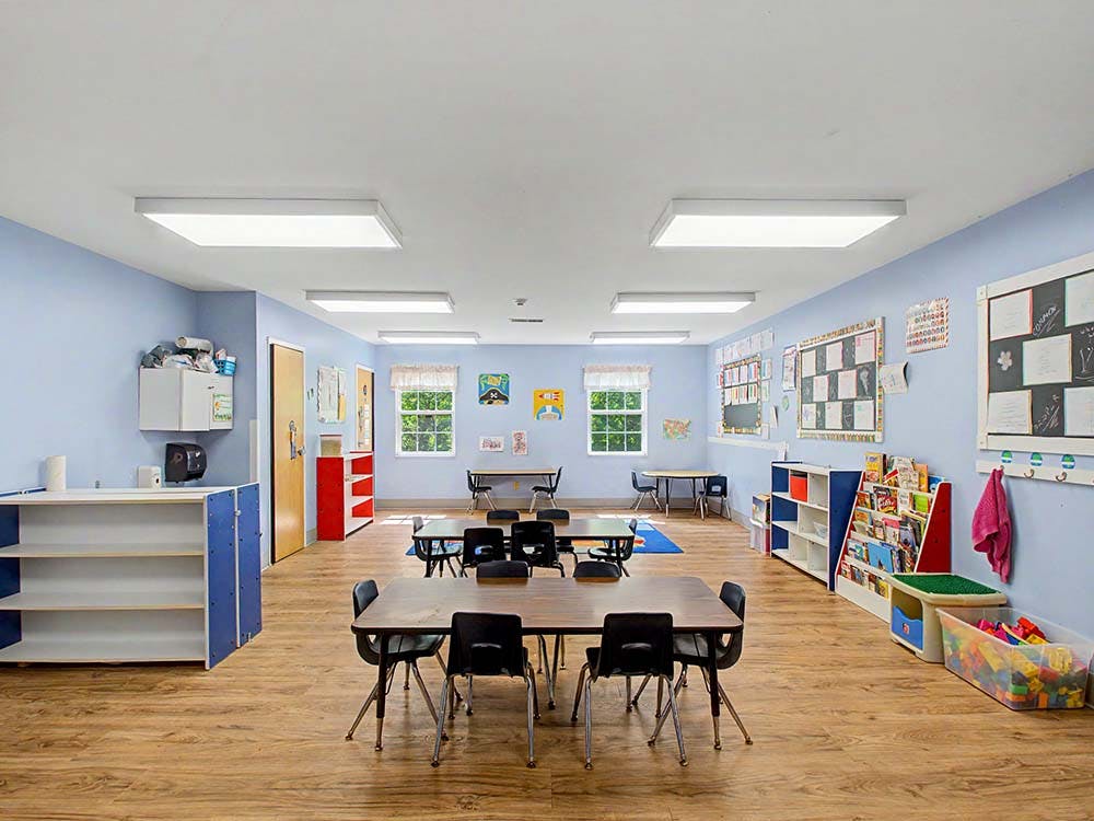 Classroom with light blue walls, desks, chairs, and shelves