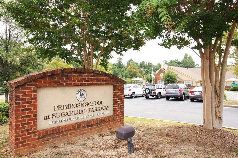 Brick sign for Primrose School at Sugarloaf Parkway with cars in background