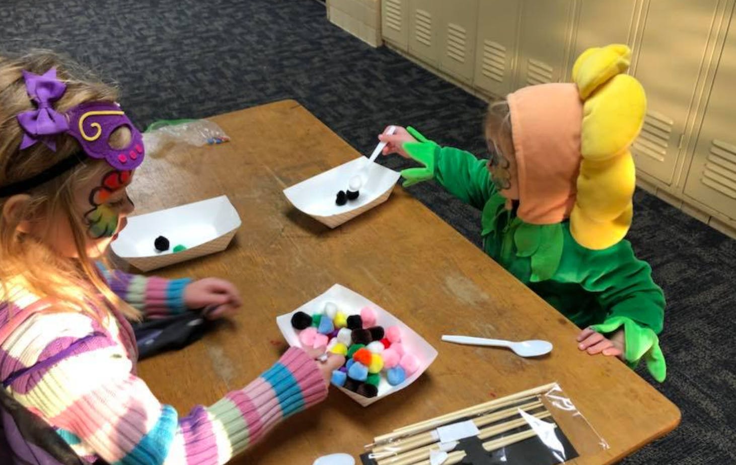 Two children at a table doing a craft with pom-poms