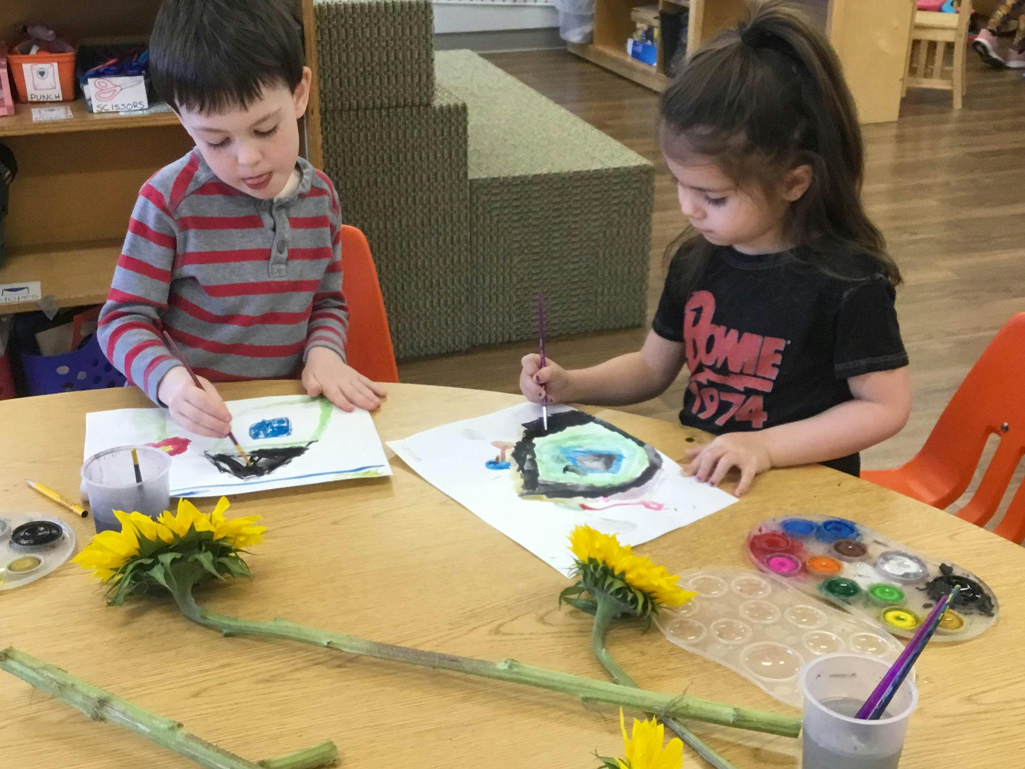 Two children painting at a table with sunflowers