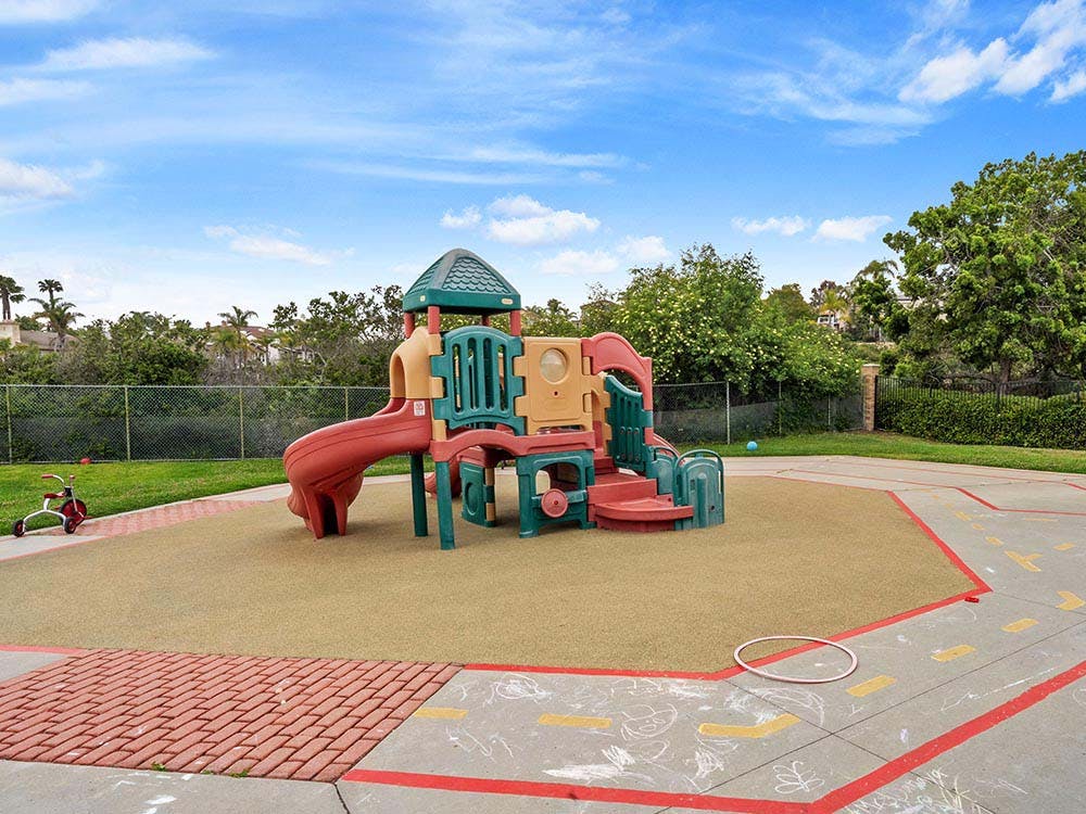 Colorful playground structure on a tan soft surface with a tricycle nearby