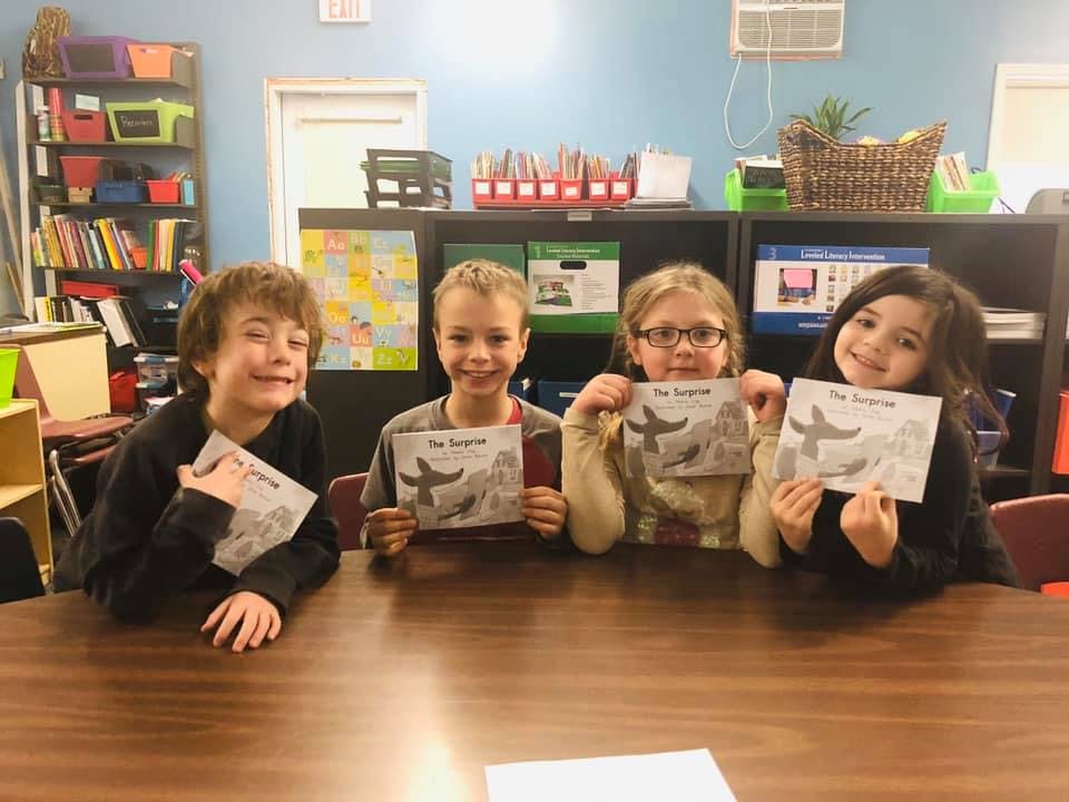 Four children holding up books in a classroom