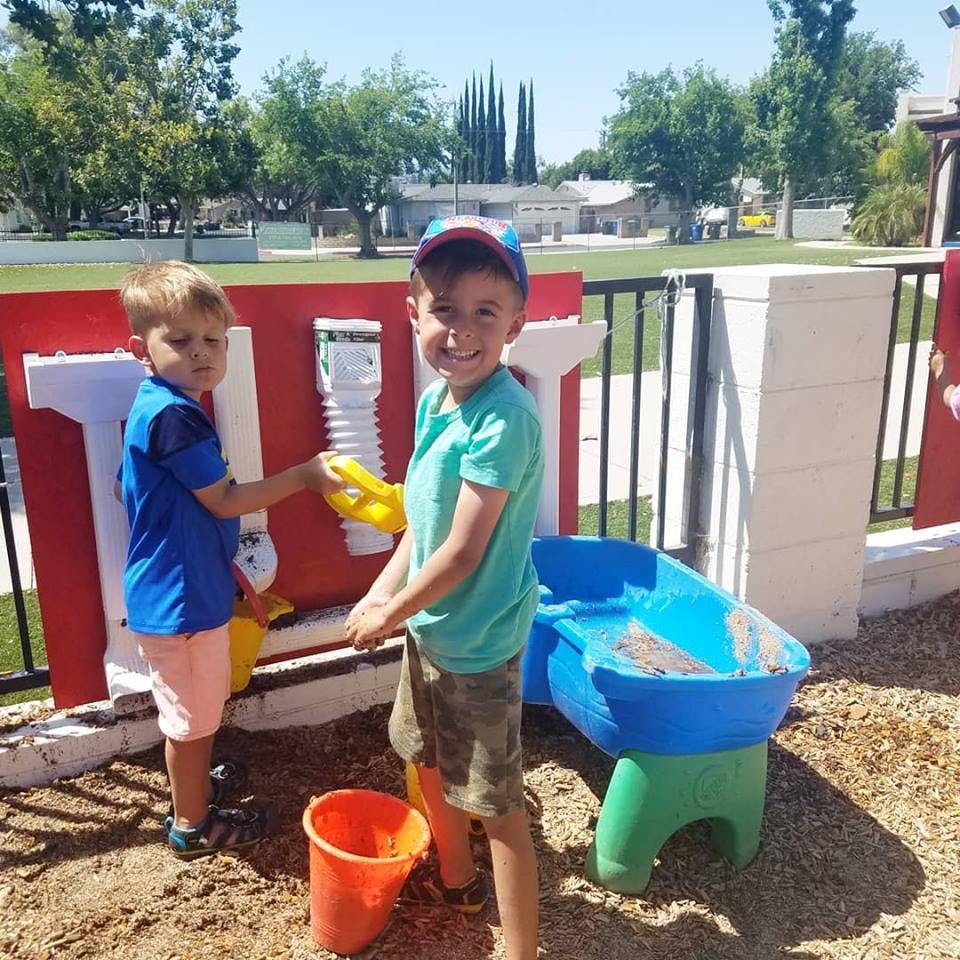 Two children playing with a water table and sand in a sandbox