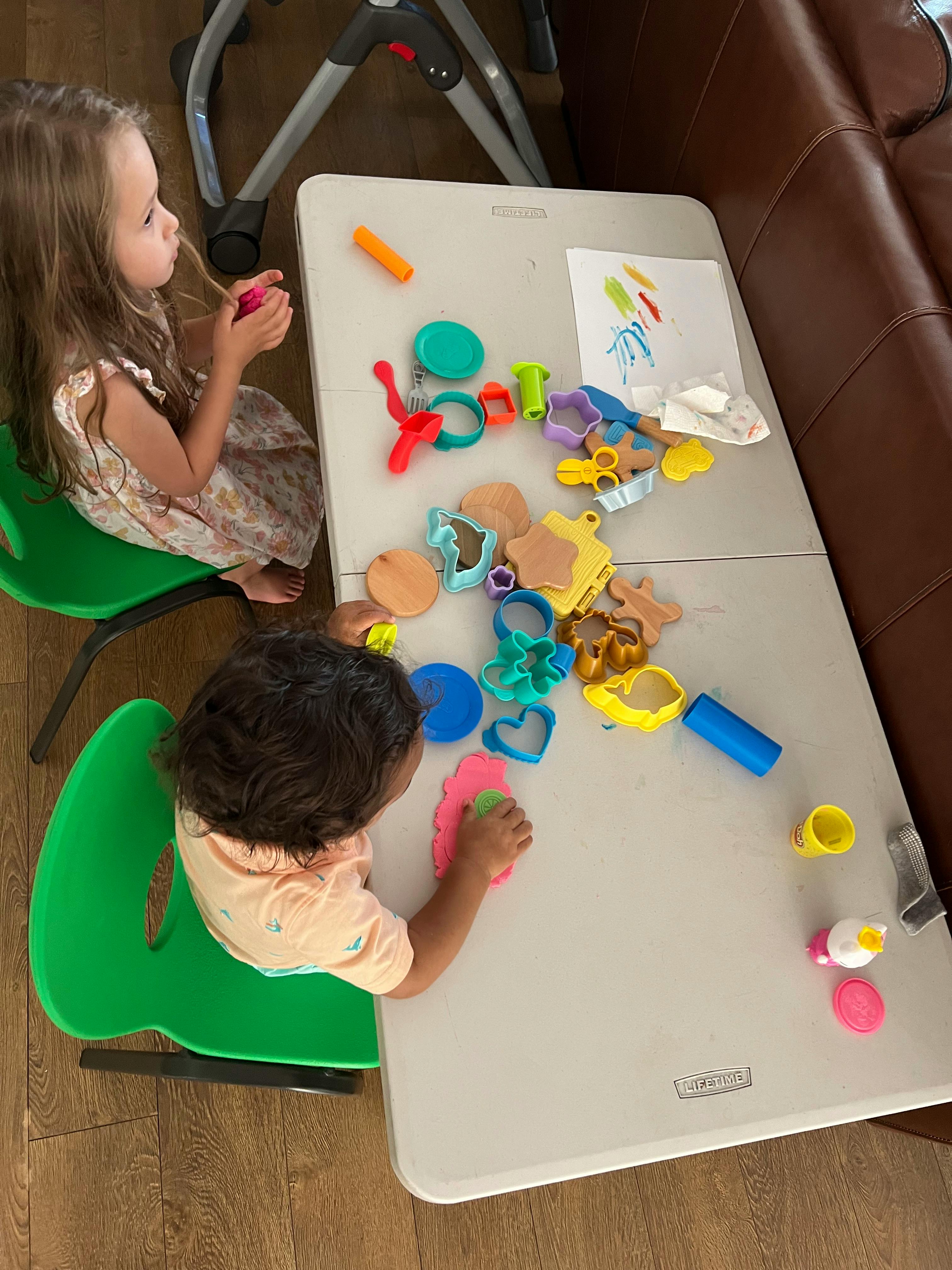 Two children playing with modeling clay and cookie cutters at a table