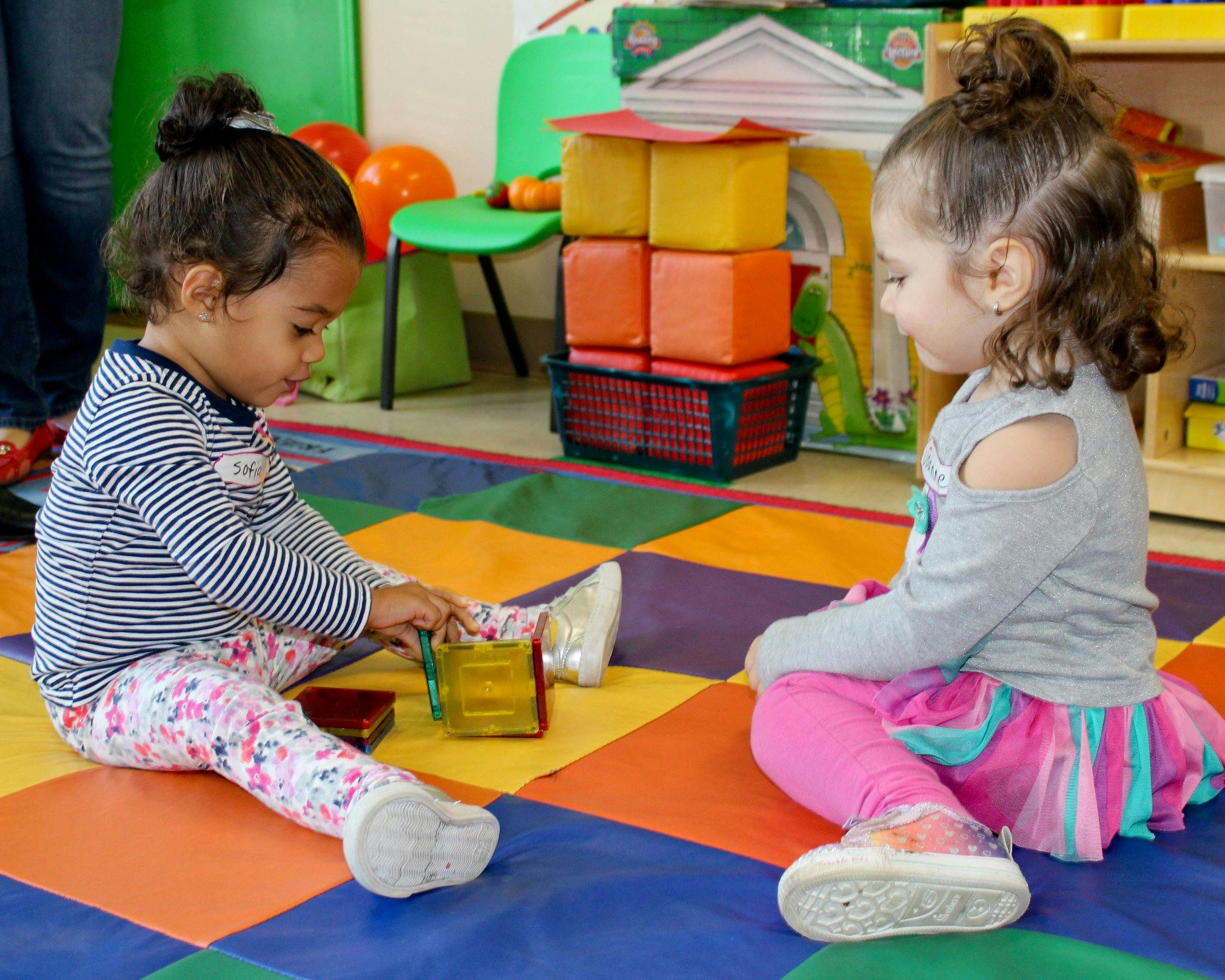 Two children sitting on a colorful mat playing with toys