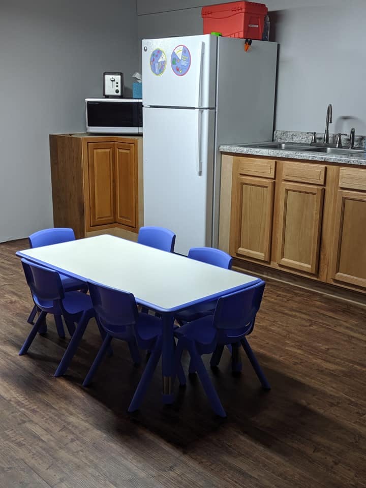 Small table with six chairs in a room with a refrigerator and cabinets
