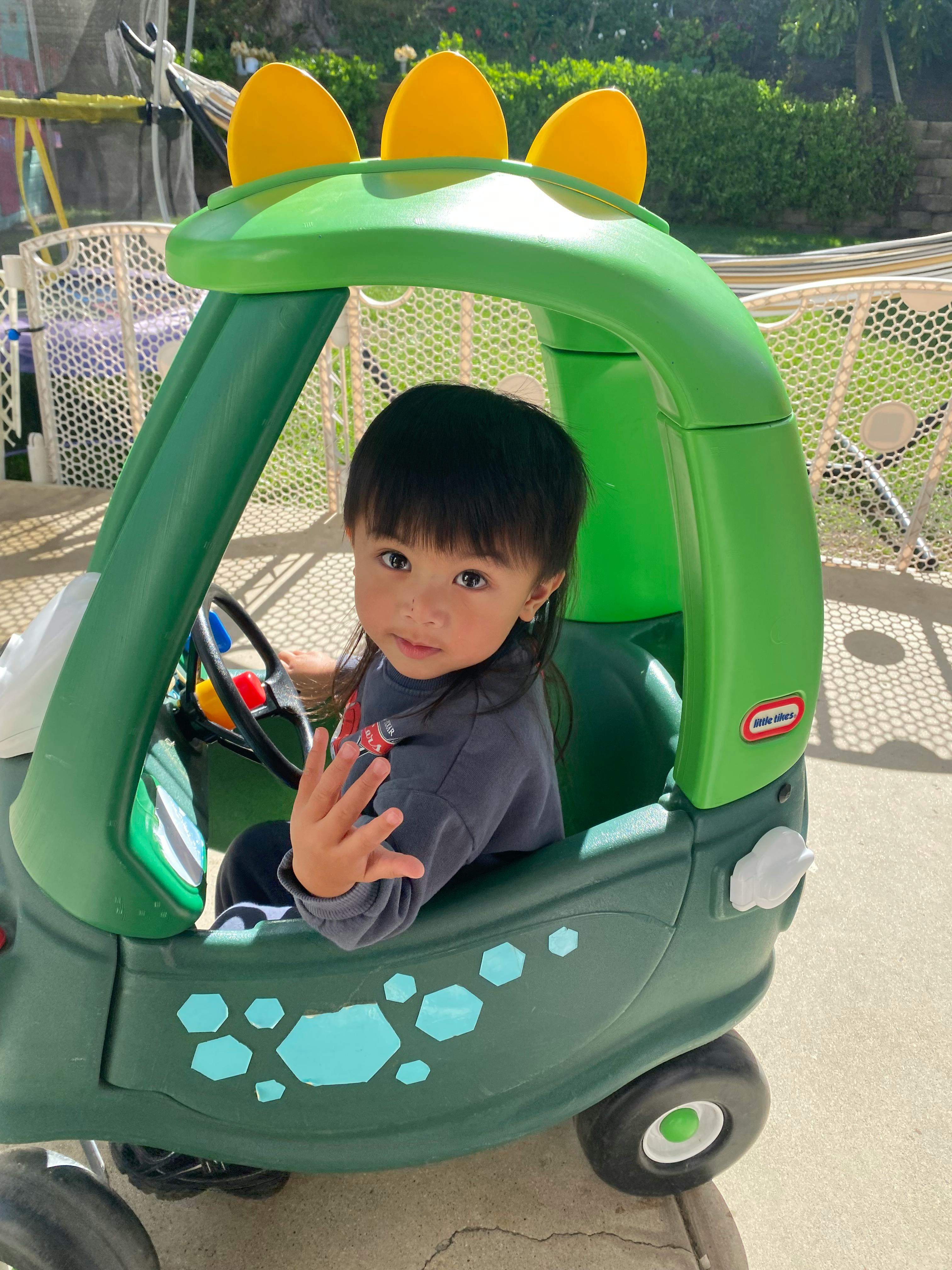 Child in a green toy car with yellow spikes