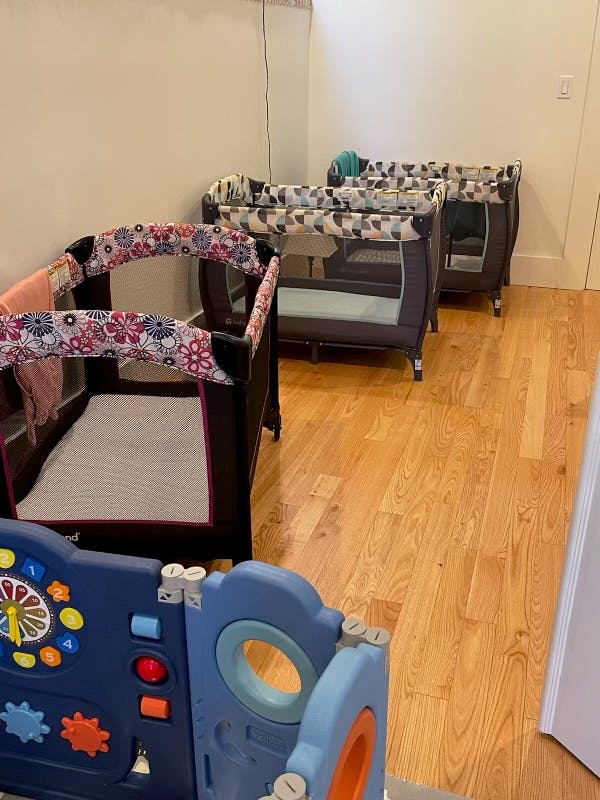 Multiple portable cribs in a room with a playpen in the foreground