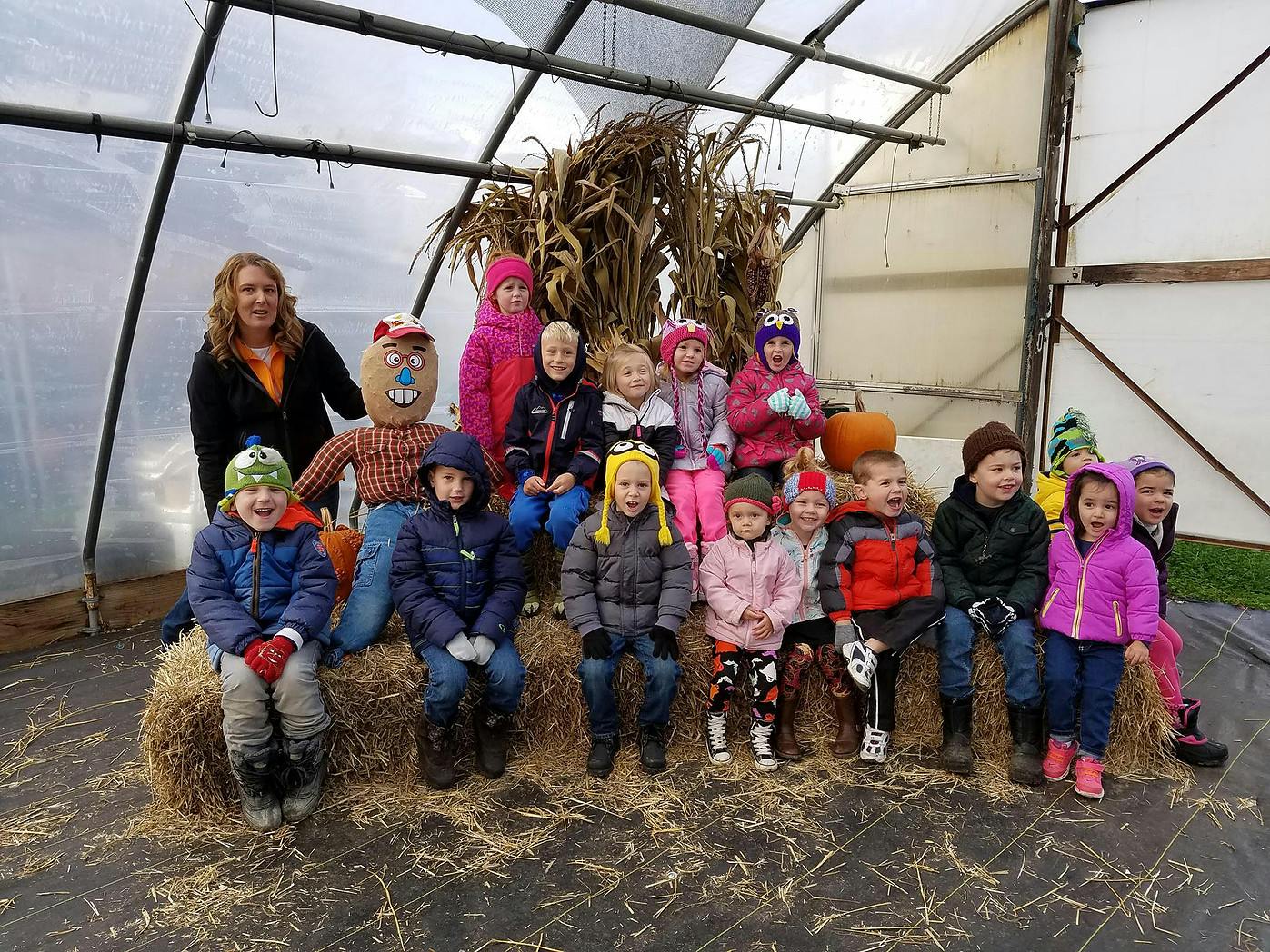 Adult and children sitting on hay bales in a greenhouse