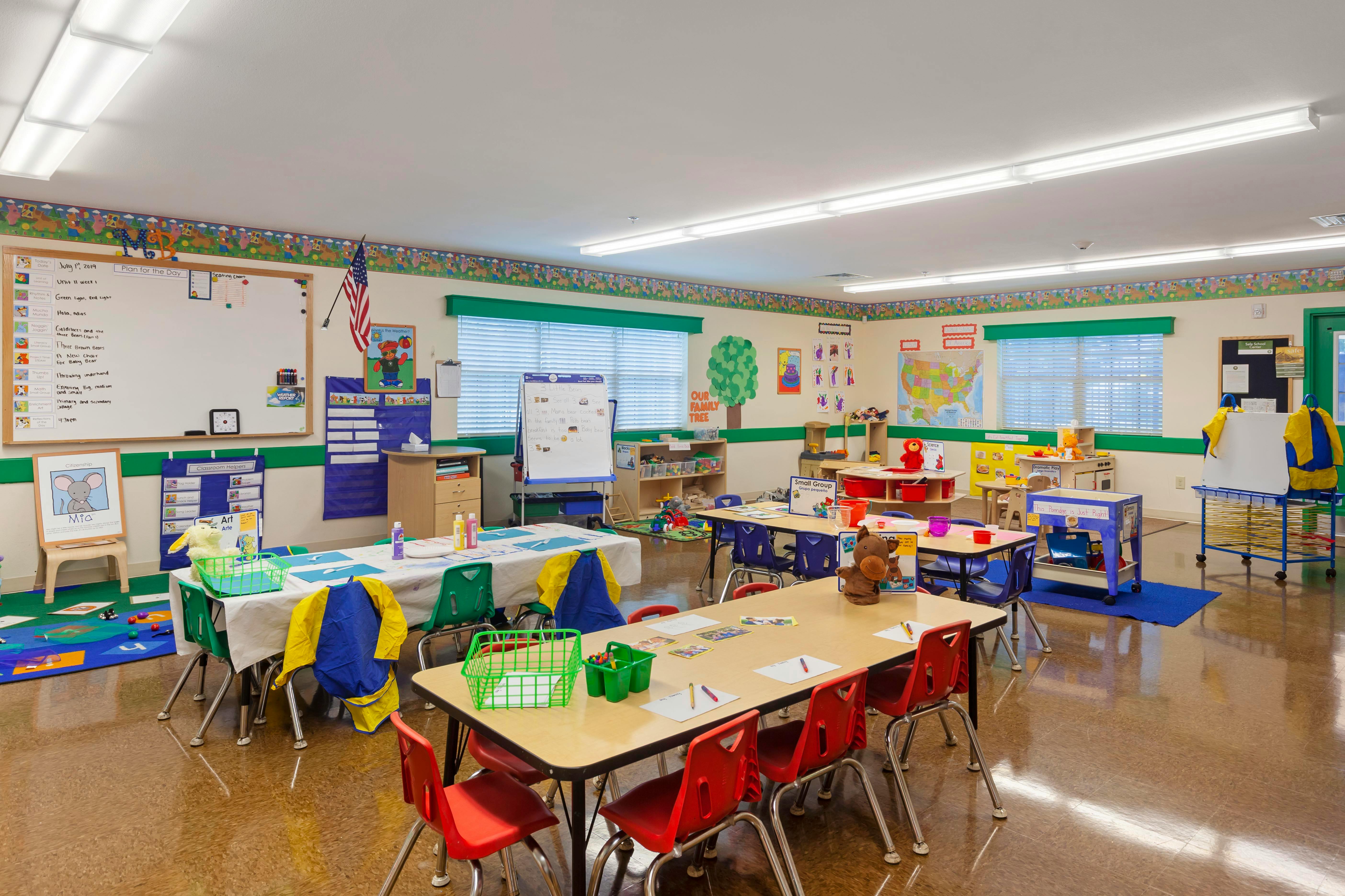An empty classroom with several small tables and chairs, a whiteboard, and educational posters