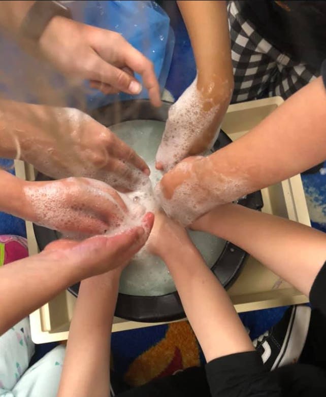 Multiple people washing hands in a basin of soapy water