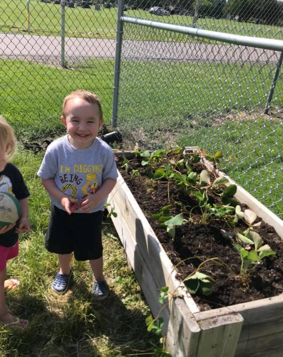 Child standing next to a raised garden bed with plants