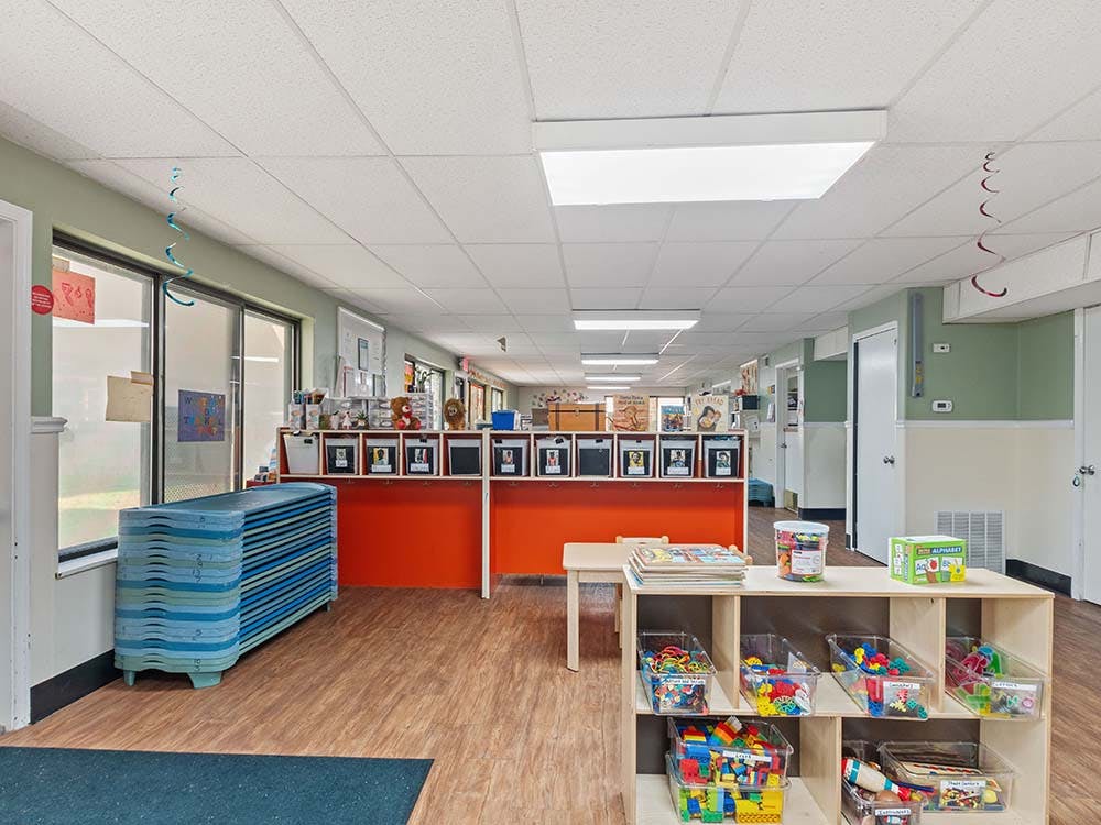 Classroom interior with cots stacked by window and toy shelves