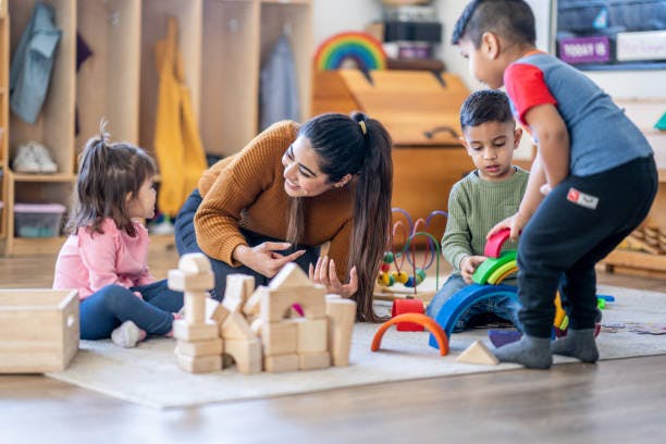 Adult and three children playing with blocks and toys on the floor
