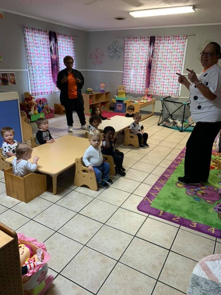 Two people standing in a room with several children seated at tables