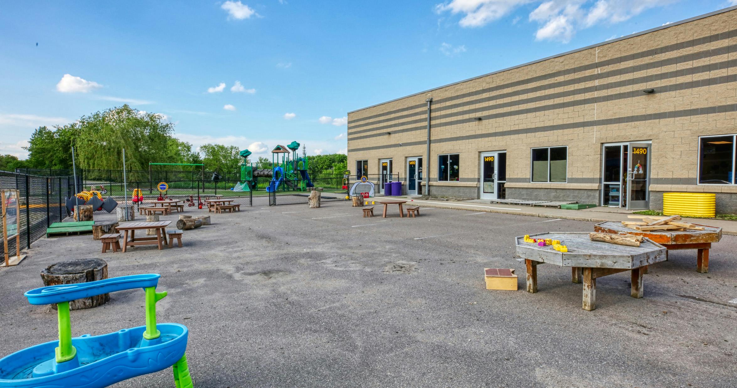 Outdoor playground area with picnic tables, tree stumps, and play structures