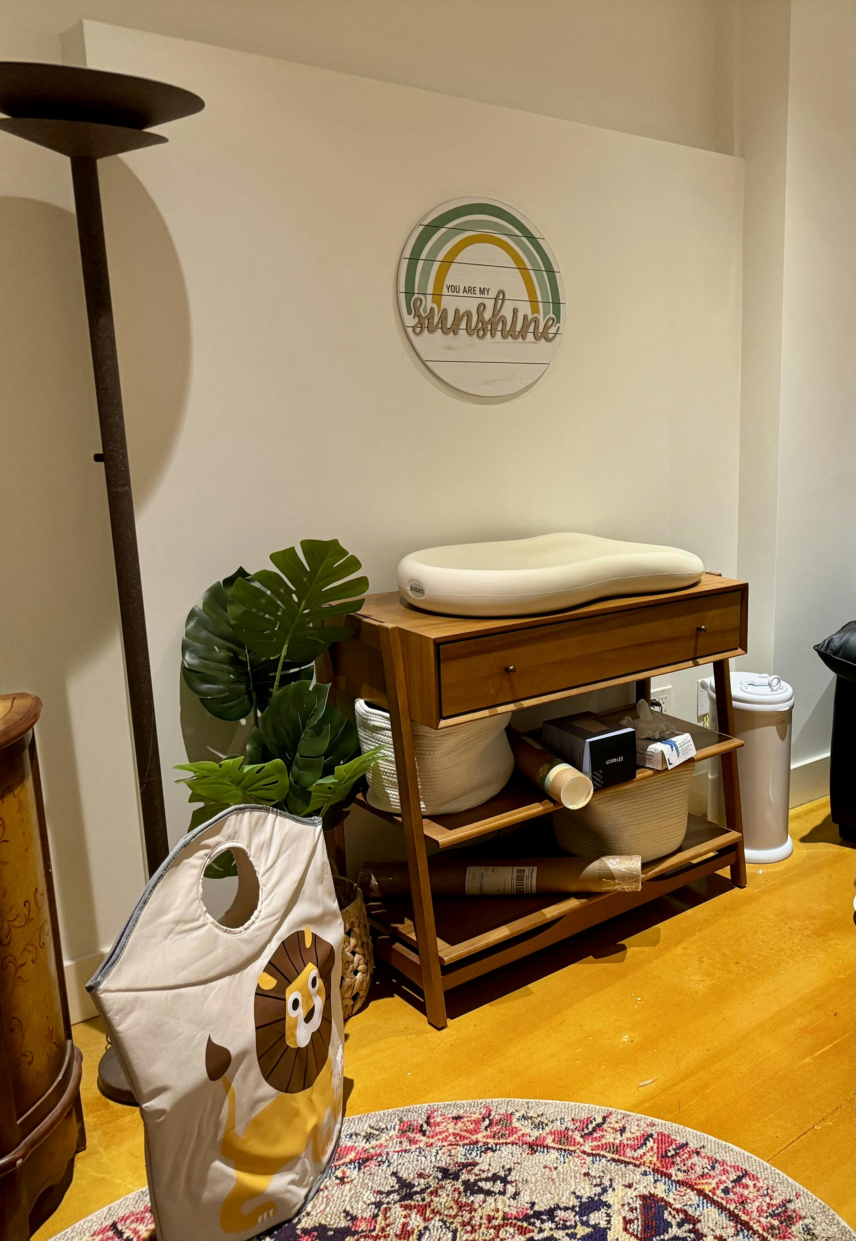 Changing table with a changing pad, plant, and a lion laundry basket