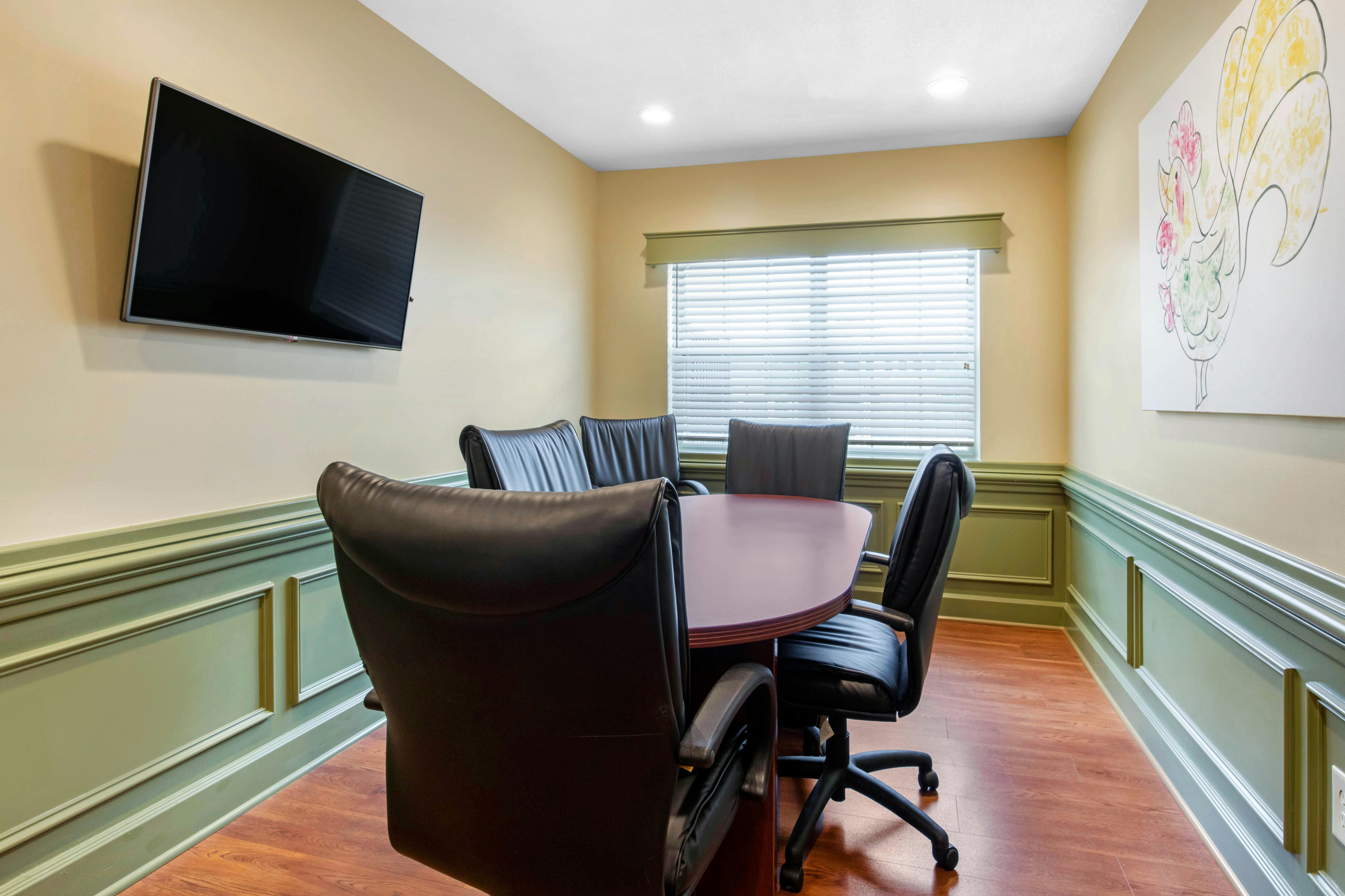 A conference room with a large screen TV, wood table, and black office chairs