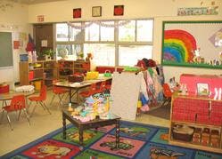 Classroom with small tables and chairs, colorful rug, and rainbow drawing