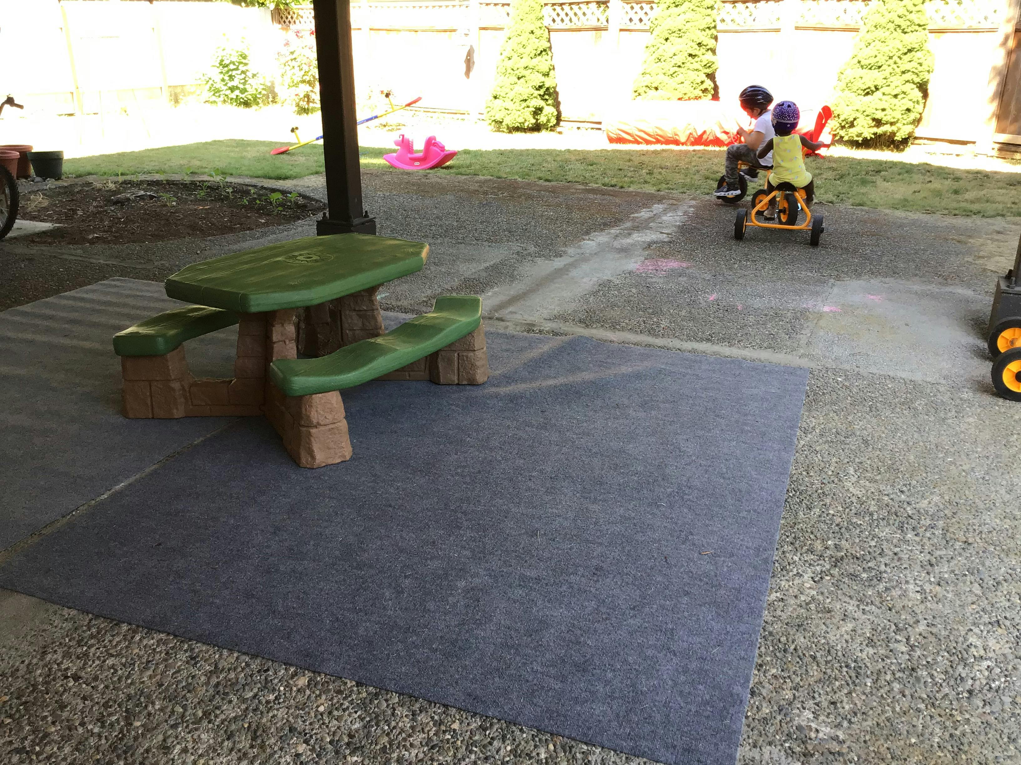 Children playing on a tricycle and a green picnic table in a yard