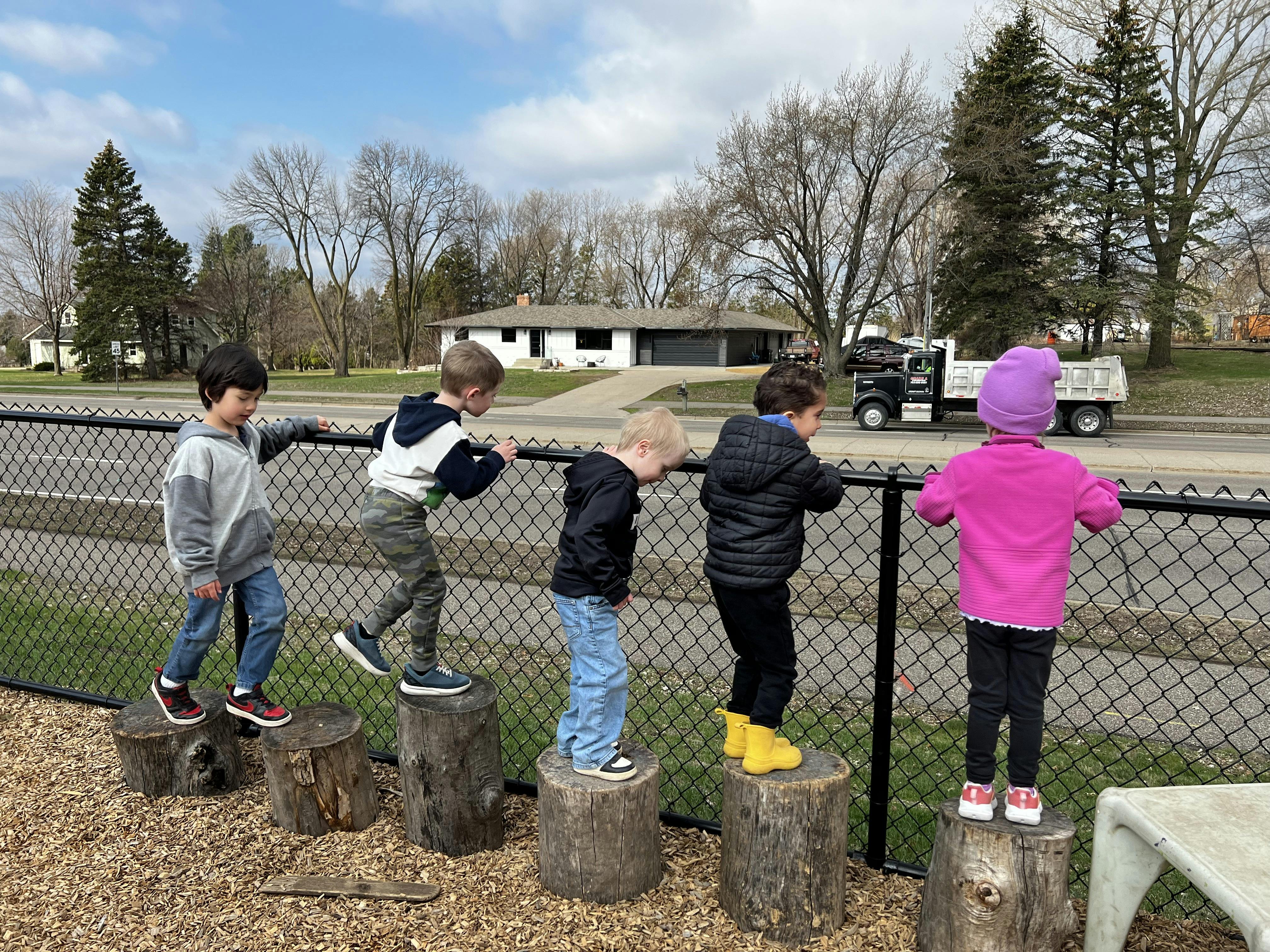Children balancing on tree stumps next to a fence