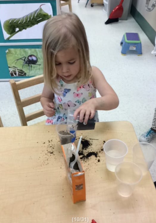Child pouring dirt from a container into a cup at a table