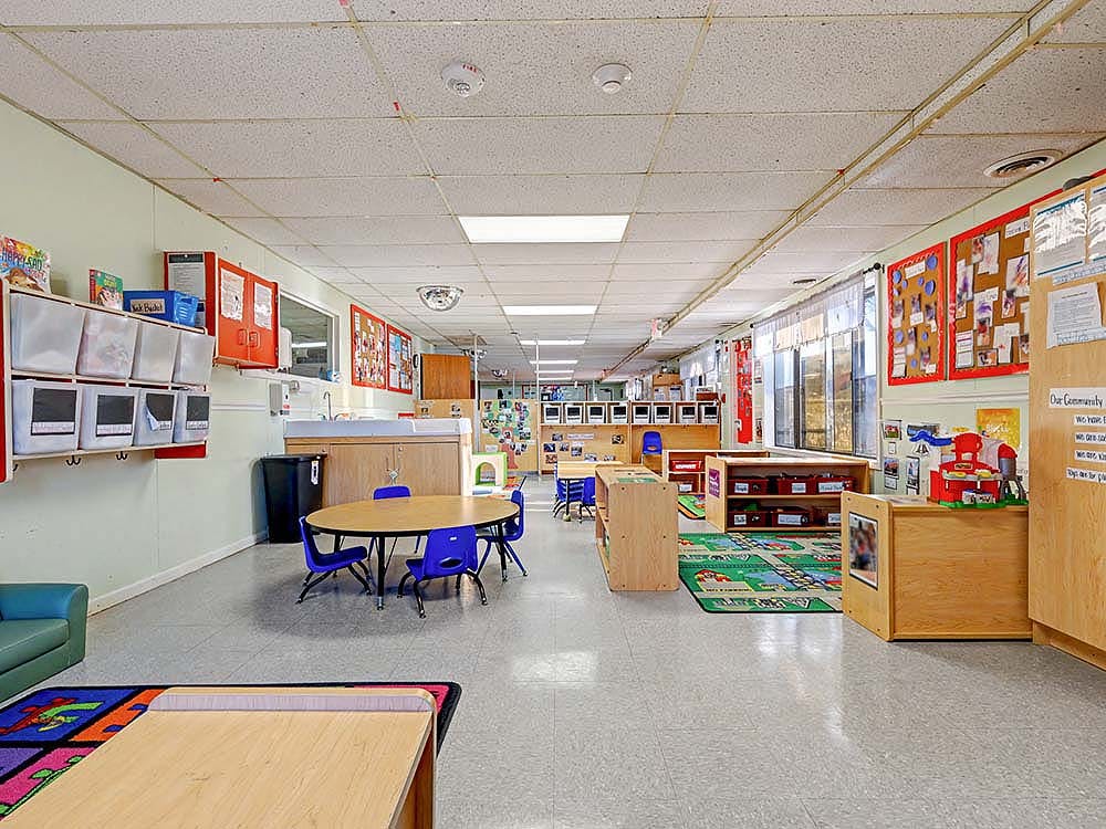 Empty colorful daycare classroom with small tables, chairs, and play areas